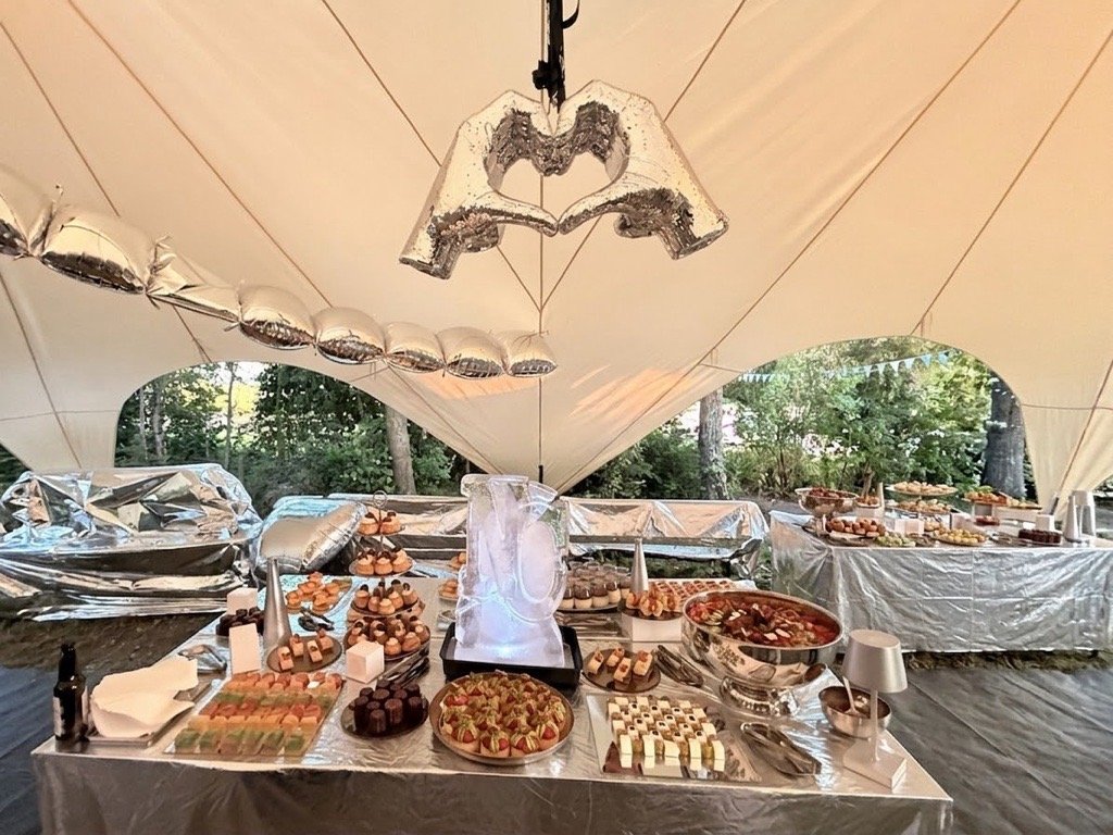 Marquee interior with silver-clad tables, a mirrored balloon heart overhead and an ice sculpture on the food table